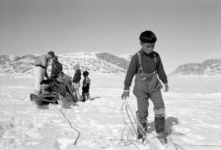 An Inuit boy preparing to set up camp in White Bay, Eclipse Sound, North West Territories, with the mountains of Baffin Island in the background. 1952. © Library and Archives Canada.